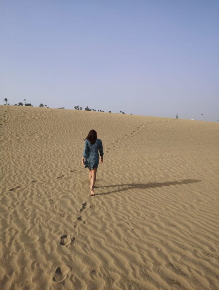 Viaggiatrice travel designer che cammina sulle dune di sabbia delle isole canarie, a Fuerteventura